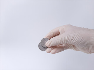 A hand in white latex glove holds money, Indonesian coins. Isolated in white background. Side view.