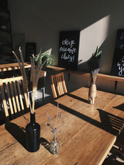 An interior of a coffee shop sun rays on the wall, wine bar, with wooden tables, dried flowers and...