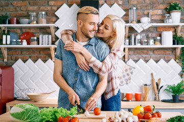Smiling young couple cooking together vegetarian meal in the kitchen at home. Woman embracing man