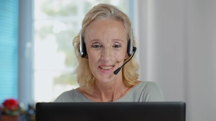Happy mature telemarketer woman with laptop attending call with headset
