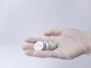 A hand in white latex glove holds money, Indonesian coins. Isolated in white background. Side view.