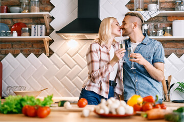 Young happy couple drinking champagne and enjoying the company of each other in kitchen at home