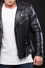 A man in a black denim jacket, a white T-shirt and blue jeans close-up in the studio on a gray background.