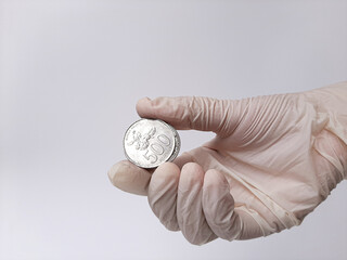 A hand in white latex glove holds money, Indonesian coins. Isolated in white background. Side view.