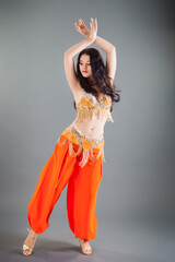 beautiful young slim brunette girl in orange belly dancer costume lifts hands up