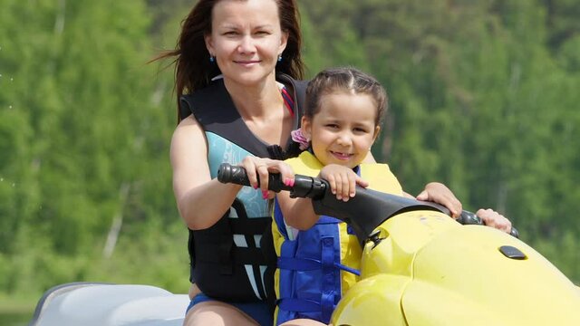 Mom and daughter ride the river on a personal watercraft, have fun and enjoy life. Sunny summer day. Slow motion