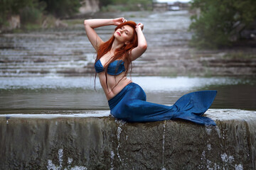 a mermaid in a blue suit with long red hair in the river  