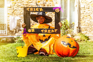 Halloween portrait of a black handsome boy in spooky costume with pumpkin hold trick or treat frame