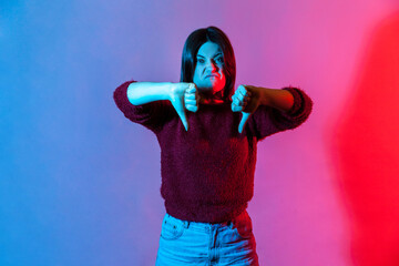 Neon light portrait of angry displeased young woman looking with disgust hate and showing thumbs down, dislike gesture, negative feedback, rejection, disapproval sign. indoor studio shot isolated