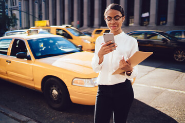 Young gorgeous African American woman in cool spectacles order online yellow ca via smartphone...