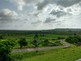 Landscape view of a agriculture field in a hilly rural area. A narrow asphalt road has gone through its side.