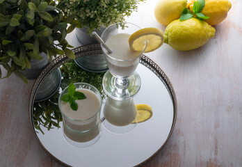 Lemon mousse with whipped cream in a clear glass, fresh lemons and spice plants on a wooden base