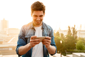 Obraz premium Photo of excited man smiling and playing online game on mobile phone