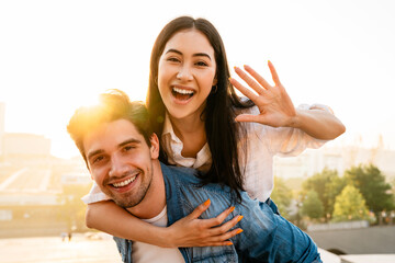 Image of cheerful couple piggybacking ride and waving hand