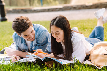 Image of joyful student couple doing homework while lying on grass
