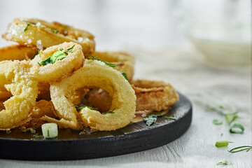 Onion rings in batter sprinkled with greens on a white background in a blur. Photo with copy space.