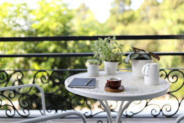 Small coffee cup with white plant pots with notebook on white table at balcony