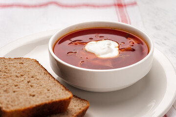 Vegetarian borscht with sour cream in a white tureen next to slices of bread on a white plate
