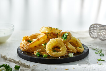 Onion rings in batter sprinkled with greens on a white background in a blur. Unhealthy but delicious food.