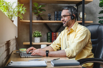 Man in front of desk with laptop computer and headset working - Powered by Adobe