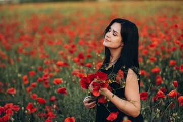 Naklejka premium Portrait of a beautiful cute brunette girl in poppy field at sunset