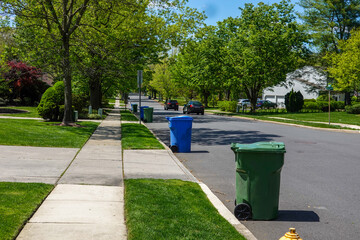 View down a residential tree lined street with green and blue trash bins lined up for collection