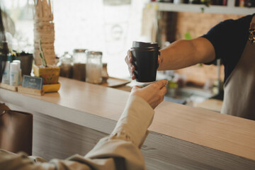 Takeaway. young friendly barista serving black hot coffee cup to female customer over counter in modern cafe coffee shop, cafe restaurant, service mind, small business owner, food and drink concept