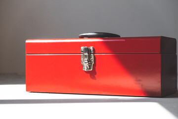 closed red tool box with a black handle on a gray background, highlight on the left. place for an inscription. lock. light and shadow from the window