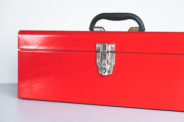 closed red tool box with a black handle on a gray background, highlight on the left. place for an inscription. lock.