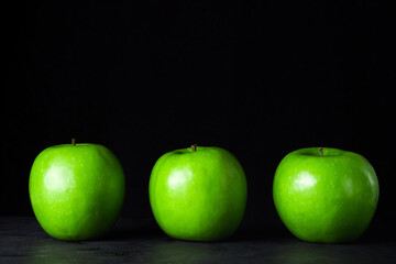 Green apples on a black background. Three apples stand in a row, next to each other.