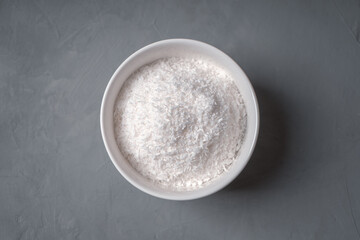 Coconut shavings in a white bowl on a concrete table top view