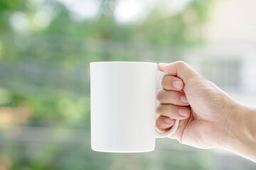 Close-up photos mock up  man's hand holds a white coffee mug, nature bokeh background.