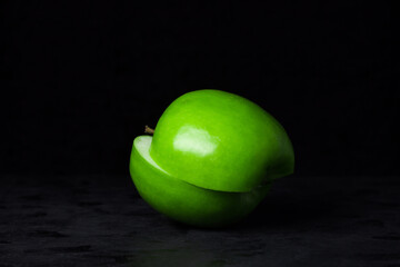 Green apple on a black background. Apple cut in half. One apple slice lies on another