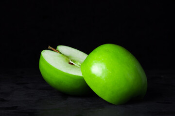 Green apple on a black background. Apple cut in half. One apple slice lies on another