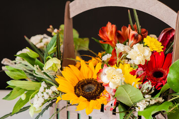 Flower arrangement with a sunflower in a basket on a black background. Stylish flowers for sale. Artistic style. Rustic style. Selective focus.