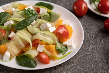 Salad of tomatoes, cheese cheese, cucumber, spinach. The dark blue background of the stone. Food for vegetarians. The concept of healthy eating.