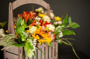 Flower arrangement with a sunflower in a basket on a black background. Stylish flowers for sale. Artistic style. Rustic style. Selective focus.