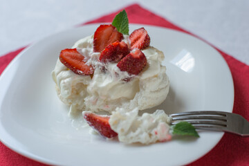 Closeup Pavlova meringue cake with whipped cream, fresh strawberry and mint on white plate. Delicious dessert.