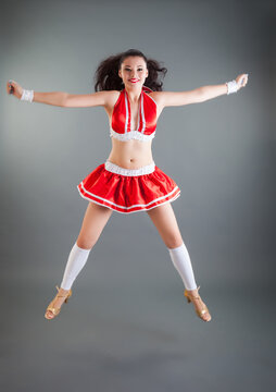 attractive young girl with long dark hair in red cheerleader costume jumps in studio