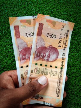 Hand holding of two two hundred rupees notes. Isolated on green background. Daylight.