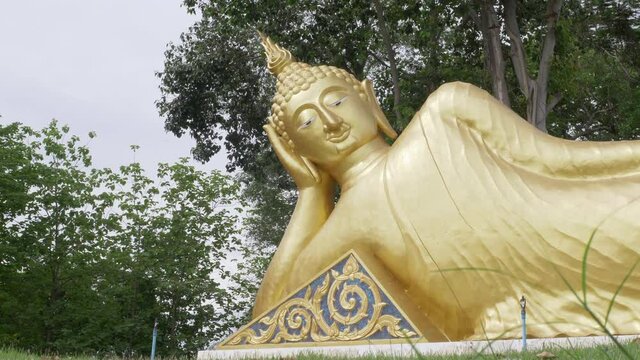 4K Big golden reclining Buddha image statue with tree nature and sky background. Travel asia Thailand.