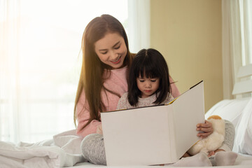 Happy family mother and daughter read a book on bed in bedroom, Asian family loving concept