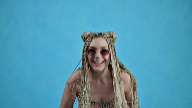 Caucasian happy woman with dreadlocks moves in the studio. Video shot on a blue background.