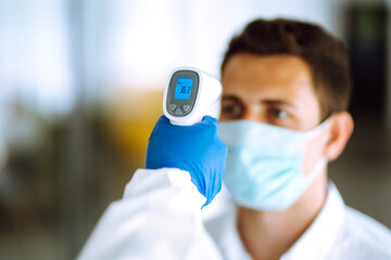 Fototapeta na wymiar Hand in glove holding ir thermometer. Medical office measurement product. Disease control experts use an Infrared thermometer equipment to check the temperature on the forehead. Covid-19.