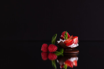 dessert of chocolate, whipped cream and fresh berries on a reflective surface, black background. the concept of a delicious summer holiday. selective focus.