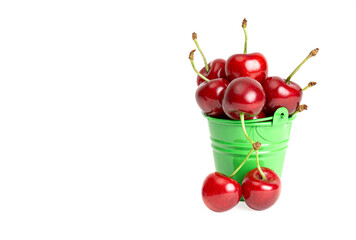 A miniature toy bucket full of ripe sweet cherries isolated on white. Closeup shot, copy space. June fruit harvesting concept.