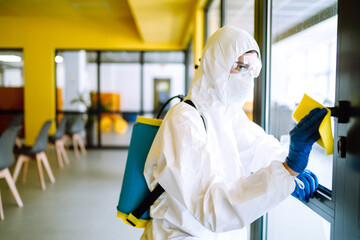 Cleaning and disinfection of office to prevent COVID-19. A disinfector man in a protective suit and...