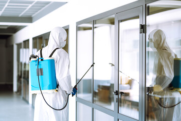 Contractor disinfecting office for COVID-19 coronavirus. A disinfector man in a protective suit and mask sprays disinfectants in office. Prevention of spreading pneumonia virus with surfaces.