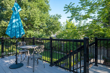 Gray PVC Deck with Black Metal Railing, a Bistro Set and Blue Sun Umbrella in a Backyard