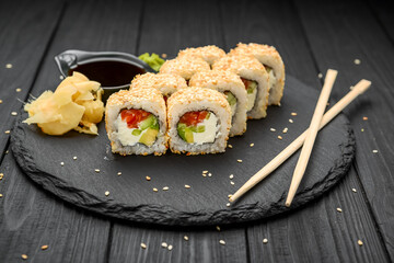 Sushi rolls in sesame with avocado, salmon and cream cheese on a black background